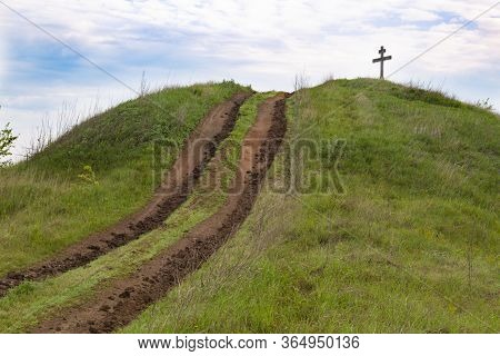 Dirt Road Going To The Top Of  Green Hill Against  Blue Cloudy Sky. Cross On Top.  Surroundings Of O
