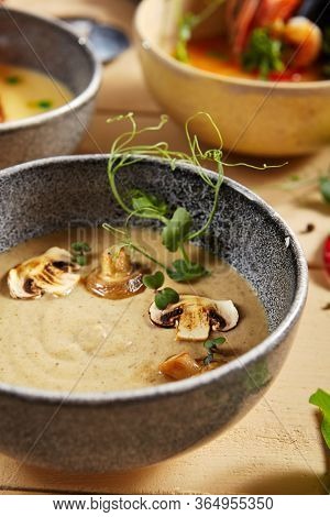 Forester soup with cheese rusks in gray bowl. Liquid dish, first course with greenery and mushrooms decoration close up. Served creamy broth, puree, mashed soup. Hot restaurant meal