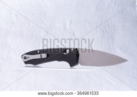 Knife With A Shiny Blade And A Clip On The Handle. Knife On A Plastic Stand In A Display Case.