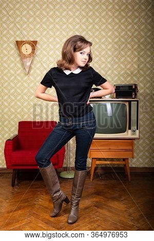 Smiling ecstatic woman looking at camera and happy smiling in room with vintage wallpaper and interior, retro stylization 60-70s. Furniture, tv set and another technique of the mid 20th century