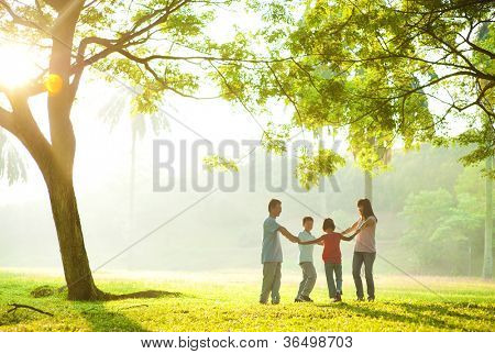 มือถือตระกูลเอเชียมีความสุขในวงกลมและการเรียกใช้งานบนสนามหญ้าสีเขียว