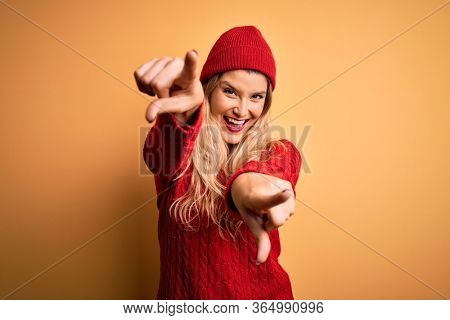 Young beautiful blonde woman wearing casual sweater and wool cap over white background pointing to you and the camera with fingers, smiling positive and cheerful