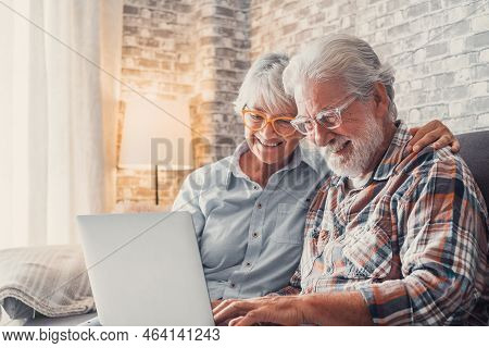 Cute Couple Of Old People Sitting On The Sofa Using Laptop Together Shopping And Surfing The Net. Tw