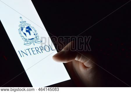 Person Holding Smartphone With Interpol Logo Displayed On Screen.