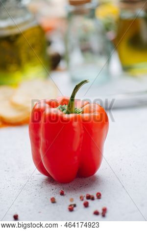 Juicy Red Paprika Pepper In Front Of Oil In Bottles Blurred In Background.
