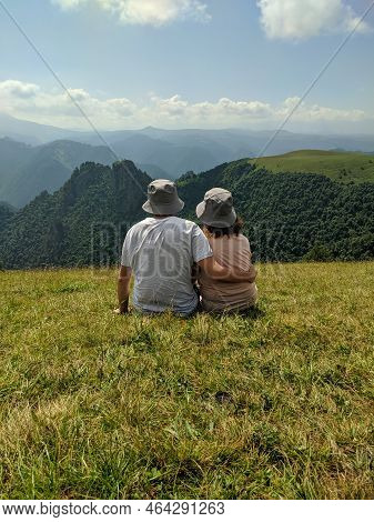 Beautiful View Of The Caucasus Mountains And Green Hills. People Sit On The Grass And Admire Nature.