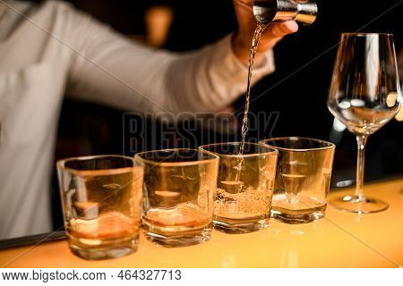 Close-up Glasses Stand On Bar And Hand Of Bartender Pours Drink From Jigger Into Glass
