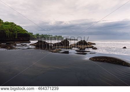 Volcanic Sandy Beach With Ocean And Waves In Balian, Bali. Beach With Rocks And Cloudy Sky