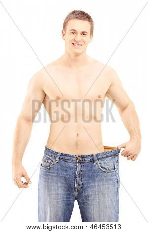 Shirtless usmívající se muž ukazuje své ztracené hmotnosti tím, že na staré džíny, izolovaných na bílém backgro