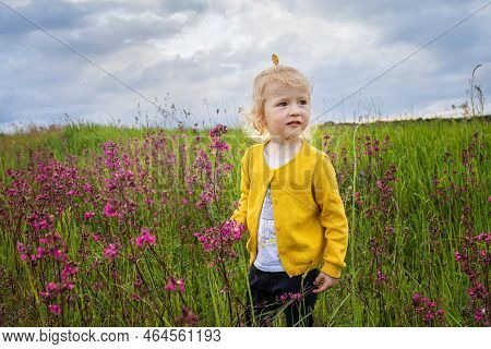 A Funny Girl In A Field With Pink Flowers. A Child In A Yellow Jacket Walks In The Evening In The Me
