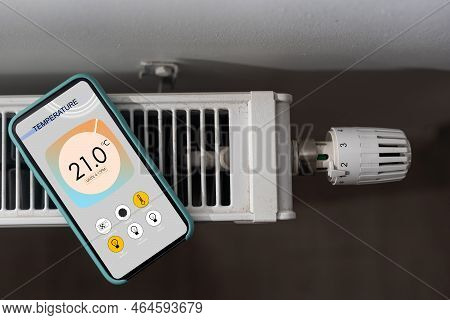 Smartphone With Launched Application For Air Temperature Adjustment Opposite The Radiator. Health Mi