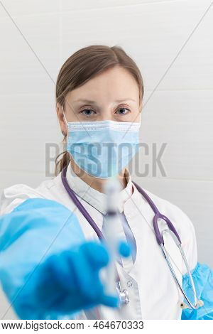 Young Woman Doctor In A Medical Mask And Gloves With A Syringe In Her Hand And A Stethoscope In A Ho