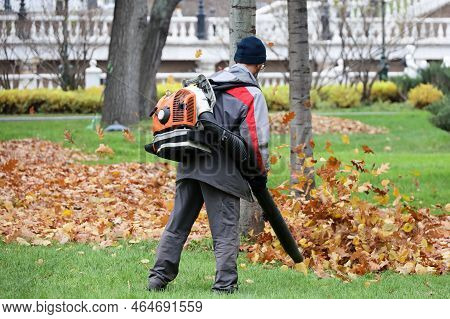 Man Worker Clean The City Street With Leaf Blower. Falling Leaves Removal In Autumn Park