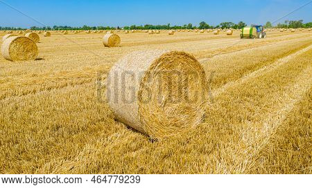 Above View Round Bale Of Straw After Harvest, In Background Tractor Is Pulling Round Baler, Machine 