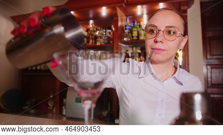 Woman Bartender With Cocktail Shaker And Glass At Bar. A Female Bartender From A Shaker Pours A Red