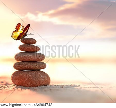 Balanced Pebble Pyramid And Butterfly On The Beach. Abstract Warm Sunset Bokeh With Sand On The Back