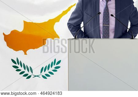 Tribune With Microphone And Man In Suit On Cyprus Flag Background. Businessman And Tribune On Cyprus