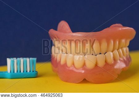 Close-up Of A Toothbrush And Removable Dentures On A Blue Background. Theme Of Dental Care And Remov