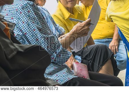 Hand Of Elderly Woman Holds A Pen To Prepare To Take Notes Of Local Community Meeting. Group Taking 