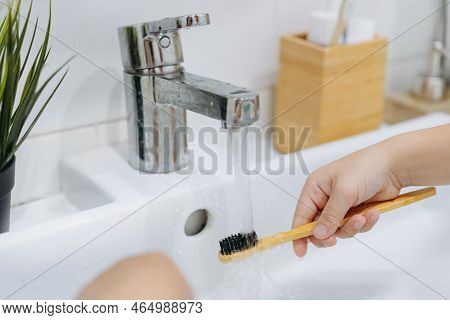 Child Is Rinsing Bamboo Tooth Brus With Water Running From Sink Tap