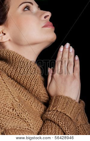 Beautiful young woman is praying. On black background.