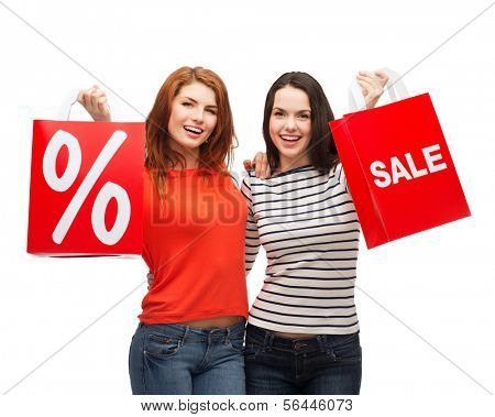 shopping, sale, and gift sconcept - two smiling teenage girls with shopping bags and percent sign