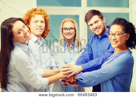 business, office, gesture and startup concept - smiling creative team with hands on top of each other sitting in office