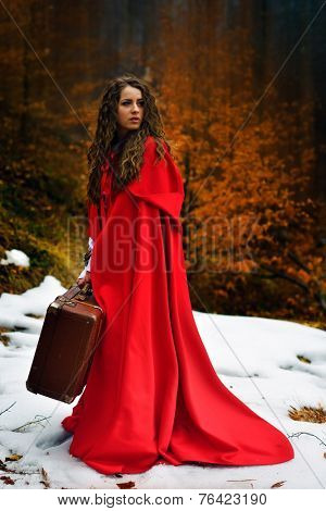 beautiful woman with red cloak and suitcase alone in the woods