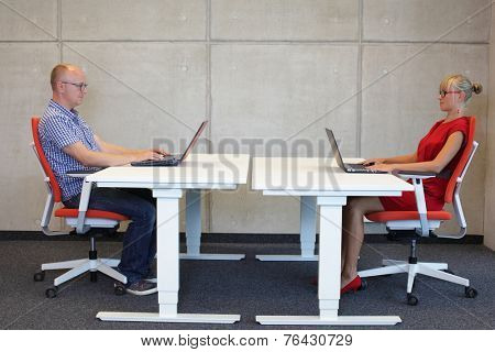 middle-aged man and young woman working in correct sitting posture with laptops  at electric height adjustable desks in office