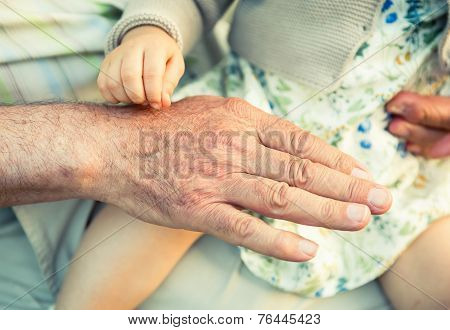 Baby girl touching hand of senior man