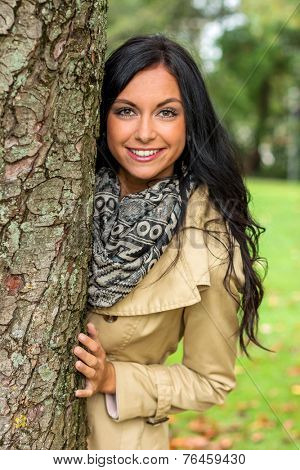 a young woman looks out from behind a tree