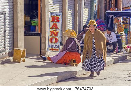 COPACABANA, BOLIVIA, MAY 6, 2014: Local woman in traditional costume and bowler hat passes by public toilet