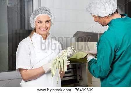 Portrait of smiling female chef holding spaghetti pasta with colleague working at commercial kitchen