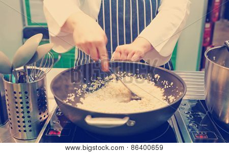 Chef is stirring risotto in a large pan, strong motion blur, toned image