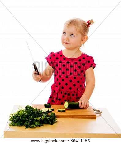 Little girl cuts a cucumber.