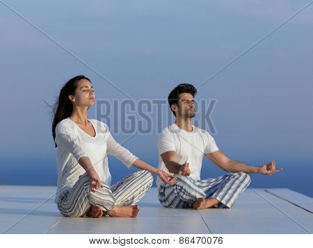 young couple practicing yoga at sunset in modern home terace with ocean and sunset in background