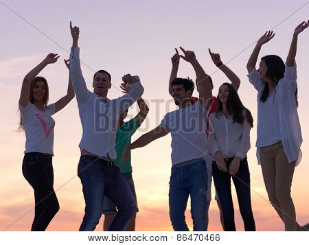 group of happy young people dancing and have fun on party in modern home bacony with sunset and ocean in background