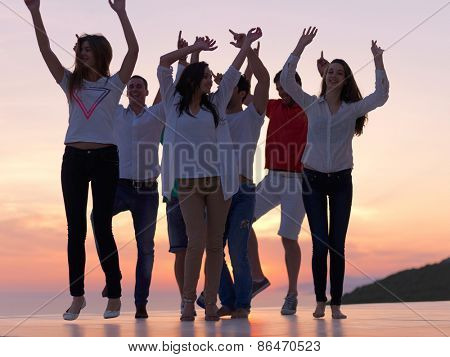 group of happy young people dancing and have fun on party in modern home bacony with sunset and ocean in background