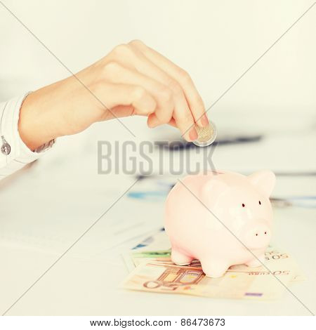 business, office, household, school, tax and education concept - woman hand putting coin into small piggy bank