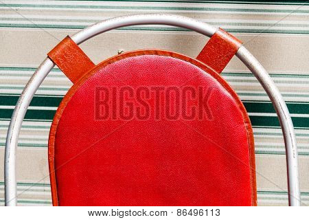 A red cushion on a chair with a metal oval frame against a background with lines