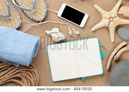 Smartphone and notepad on sea sand with starfish and shells. Top view with copy space