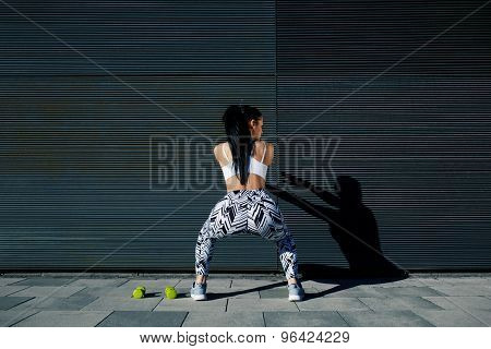 Rear view fit female in sportswear squatting after training on black background outdoors