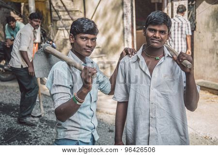 MUMBAI, INDIA - 08 JANUARY 2015: Two young Indian workers stand in street with hoe's in hands. Post-processed with grain, texture and colour effect.