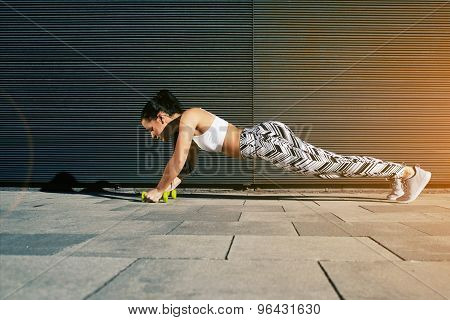 Sporty female in workout gear doing push-ups with some weights against wall with copy space