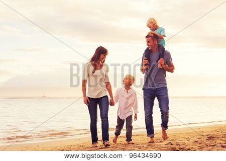 Happy young family having fun walking on the beach at sunset
