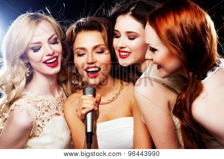 Four beautiful stylish girls singing karaoke at the club