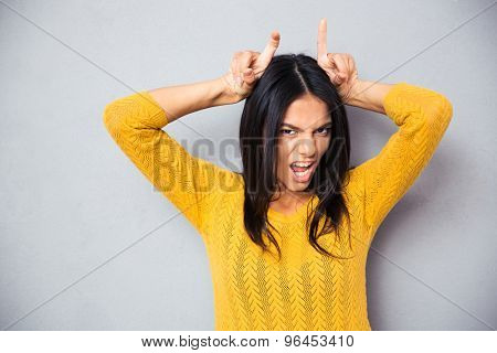 Woman showing horns with her fingers over gray background