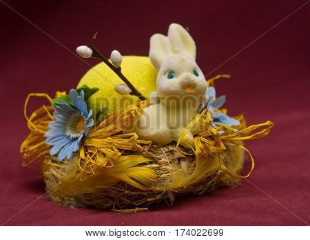 Cute white bunny sitting in a basket with flowers and colorful easter eggs