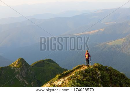 Sporty girl with back sack is standing at the edge of the precipice and watching on the endless vast of mountains landscape in the sunny day.