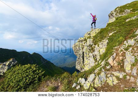 Sporty girl with back sack is standing at the edge of the precipice and watching on the endless vast of mountains landscape in the sunny day.